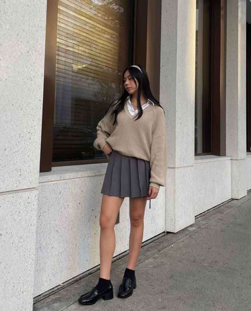 스웨터와 스커트를 입은 여성이 벽 옆에 서 있는 모습 배경화면