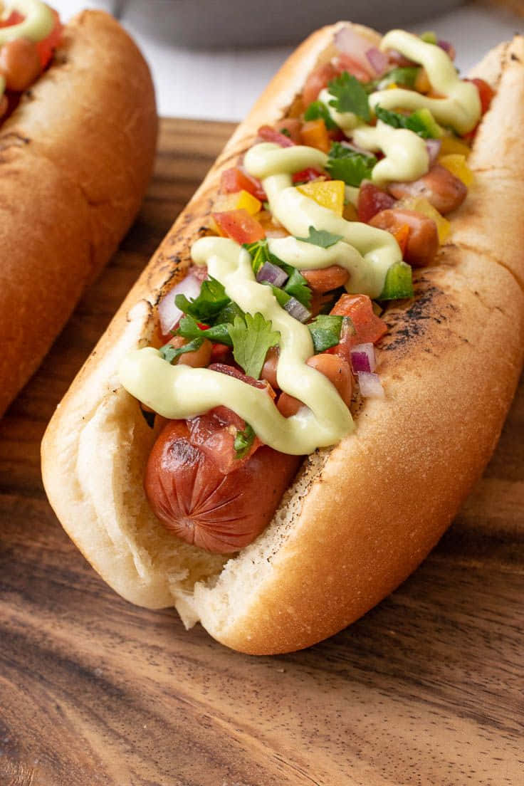 토핑이 얹어진 핫도그 두 개가 나무 도마 위에 놓여 있는 배경화면