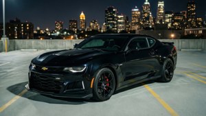 검은색 Camaro ZL1이 야간에 도시 스카이라인이 보이는 루프탑 주차장에 주차되어 있습니다. 배경화면