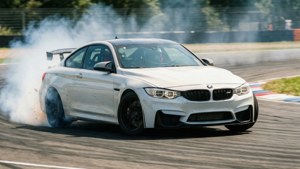 흰색 BMW M4가 타이어 연기와 모션 블러를 일으키며 서킷의 커브를 드리프트로 주행하고 있습니다. — BMW 배경화면