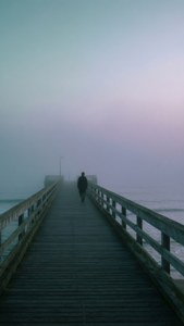새벽 안개 속 부두에 홀로 선 인물, 차분한 청록색과 라벤더 색조. — 감성 아트 배경화면