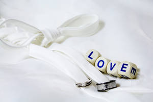 흰색 시트 위에 흰색 리본으로 묶인 은색과 검은색 웨딩 반지 옆에 'Love'라고 적힌 네 개의 흰색 주사위